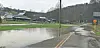 Flooded road with standing water and buildings in the background.