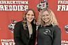 Two women smiling in front of a red Fredericktown Freddies banner.