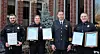 Four police officers holding certificates outside a building.
