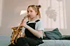 Girl playing saxophone on a bed with shadows on the wall.