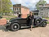 Woman in black dress next to a vintage convertible car.