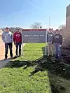 Four students in casual attire stand by a university sign.