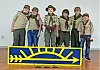Six scouts in uniforms pose together in front of a colorful backdrop.