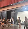 Students rehearsing a scene on stage with a wheelchair present.