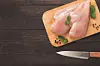 Raw chicken breasts on a cutting board with mint leaves.