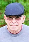 Elderly man with glasses and a cap outdoors.