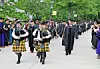 Graduates in caps and gowns with bagpipers in a procession.