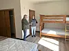Two people talking in a room with a bunk bed and mattresses.