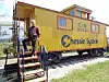 Man sitting on steps of a yellow caboose.