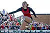Female athlete jumping over a hurdle at a track event.