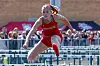 Female athlete jumping over hurdles in a red uniform.