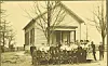 Group photo in front of a schoolhouse with students and teachers.