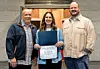 Three individuals pose with an award certificate.