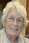 Elderly woman with glasses smiling in a casual setting.