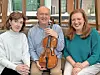 Three musicians posing indoors with a violin.