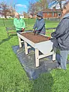 Three individuals working on a raised garden bed in a park.