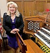 Musician beside a church organ with visible keys and pipes.