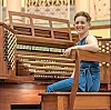 Musician seated at a grand organ, smiling.