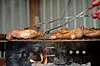 Hand using tongs to grill chicken over an open flame.