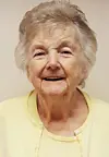 Elderly woman smiling in a yellow cardigan.