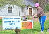 Volunteer digging at Habitat for Humanity site with signs in background.