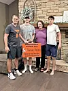 Family poses with scholarship award sign in a living room.