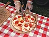 A person cutting a pizza on a checkered tablecloth.