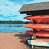 Stacked kayaks by a lake under a blue sky