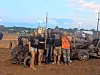 Group of four people posing with a damaged vehicle at a demolition derby.