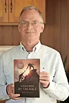 Author holding 'Coached by the Bible' book in a cozy interior.