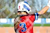 Softball player in red jersey raises arm on the field.