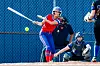 Softball player swings at a pitch with two players and an umpire in the background.