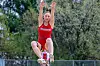 Female athlete jumping in a red uniform at a track event.