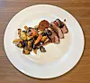 Grilled steak with roasted vegetables on a white plate.