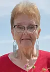 Elderly woman in a red shirt with floral earrings outdoors.