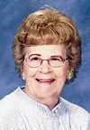 Elderly woman smiling in a light sweater with glasses.