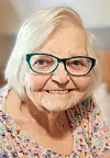 Elderly woman with glasses smiling at the camera.
