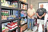 Two volunteers in a food pantry with shelves of food.
