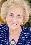 Elderly woman with curly hair smiling outdoors.