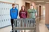 Three students stand in a school hallway beside a bench.