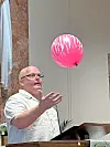 Man reaching for a pink balloon in a church.