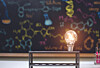 Glowing light bulb on a stand with a chalkboard in the background.