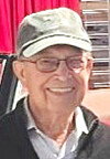 Elderly man smiling in a cap with a red background.