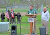 Speakers at a podium during a ceremony with flags in the background.