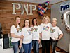 Group of five women in PWP shirts posing in an office setting.