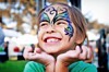 Smiling girl with butterfly face paint at an outdoor event.