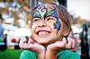 Smiling girl with butterfly face paint at an outdoor event.