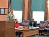 Courtroom scene with a speaker and two seated individuals.