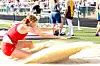 Female athlete in red jumps into a sand pit.