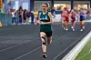 Runner in green uniform leading a race on a track.